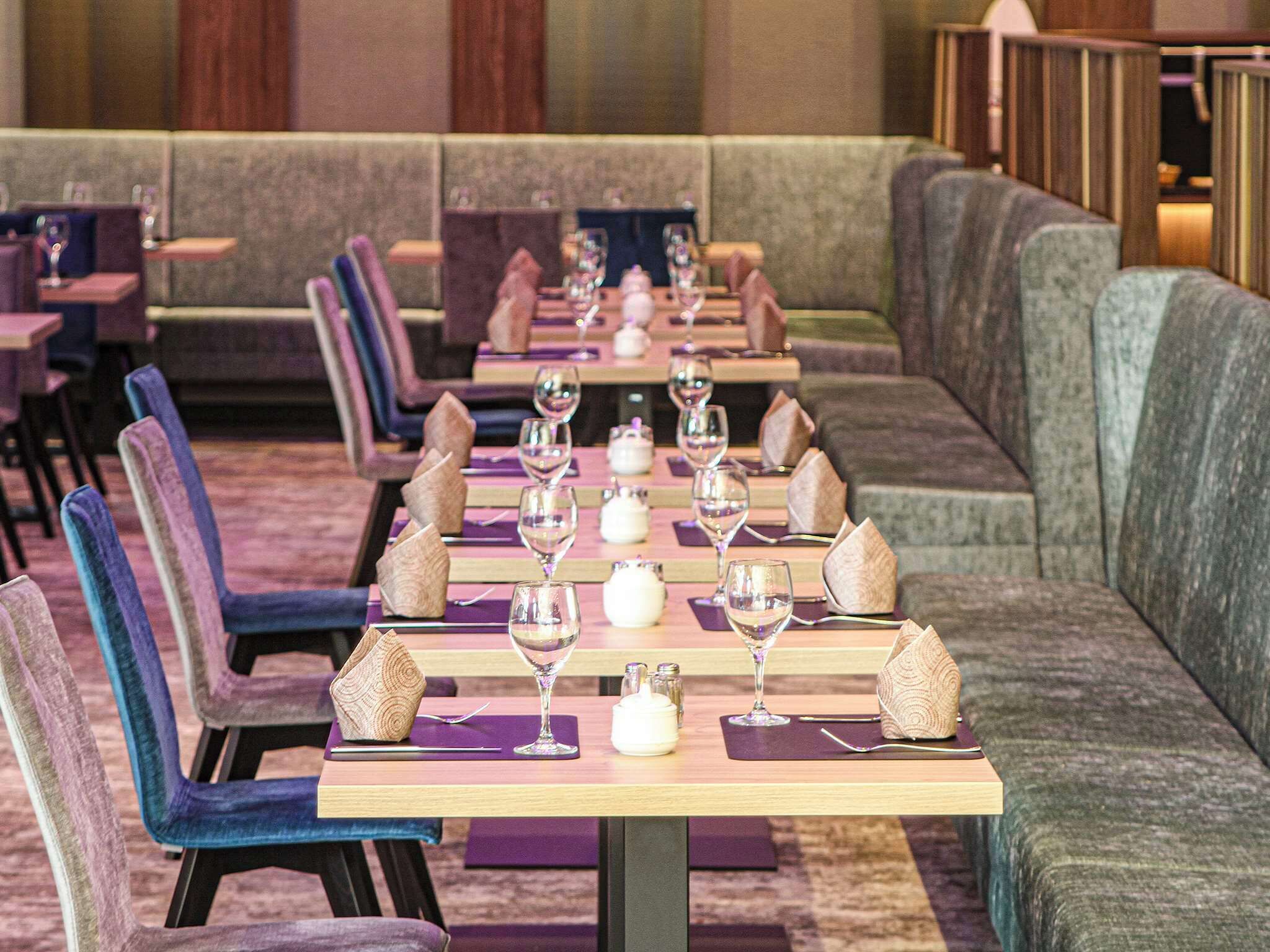 Un restaurante con largas mesas dispuestas para comer, cada una con una copa de vino, servilleta y cubiertos.