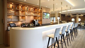 Un área de bar moderna con una barra larga, taburetes y estantes llenos de botellas y copas.