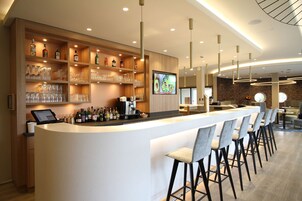 Un área de bar moderna con una barra larga, taburetes y estantes llenos de botellas y copas.