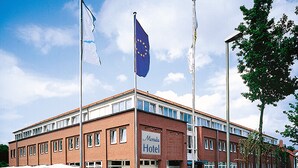 Un hotel con fachada de ladrillo rojo, varias ventanas y banderas, incluyendo la bandera de la Unión Europea.