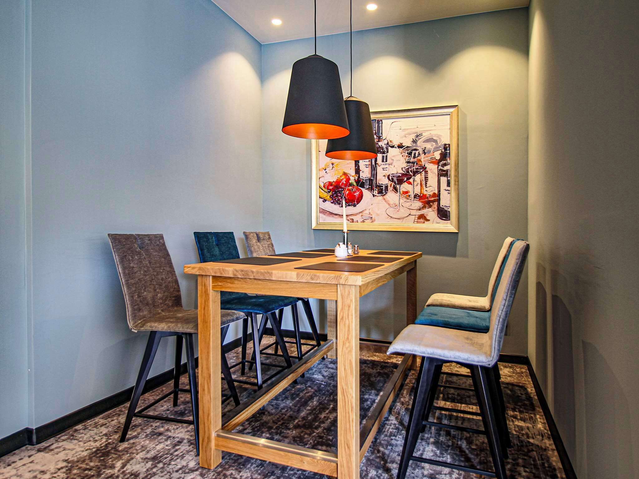 A dining area with a wooden table and chairs, a pendant light, and a framed painting on the wall.