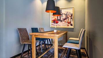 A dining area with a wooden table and chairs, a pendant light, and a framed painting on the wall.