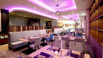 A modern restaurant with a cozy seating area, including booths and tables, and a bar in the background.