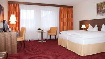 A hotel room with a large bed, two chairs, a small table with a lamp, and a desk with a lamp.