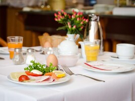 A breakfast table set with plates of food, a pitcher, salt and pepper shakers, a vase with flowers, and glasses of orange juice.