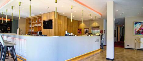 A modern hotel reception area with a curved counter, wooden paneling, and a flat-screen TV.
