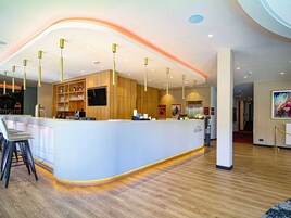 A modern hotel reception area with a curved counter, wooden paneling, and a flat-screen TV.