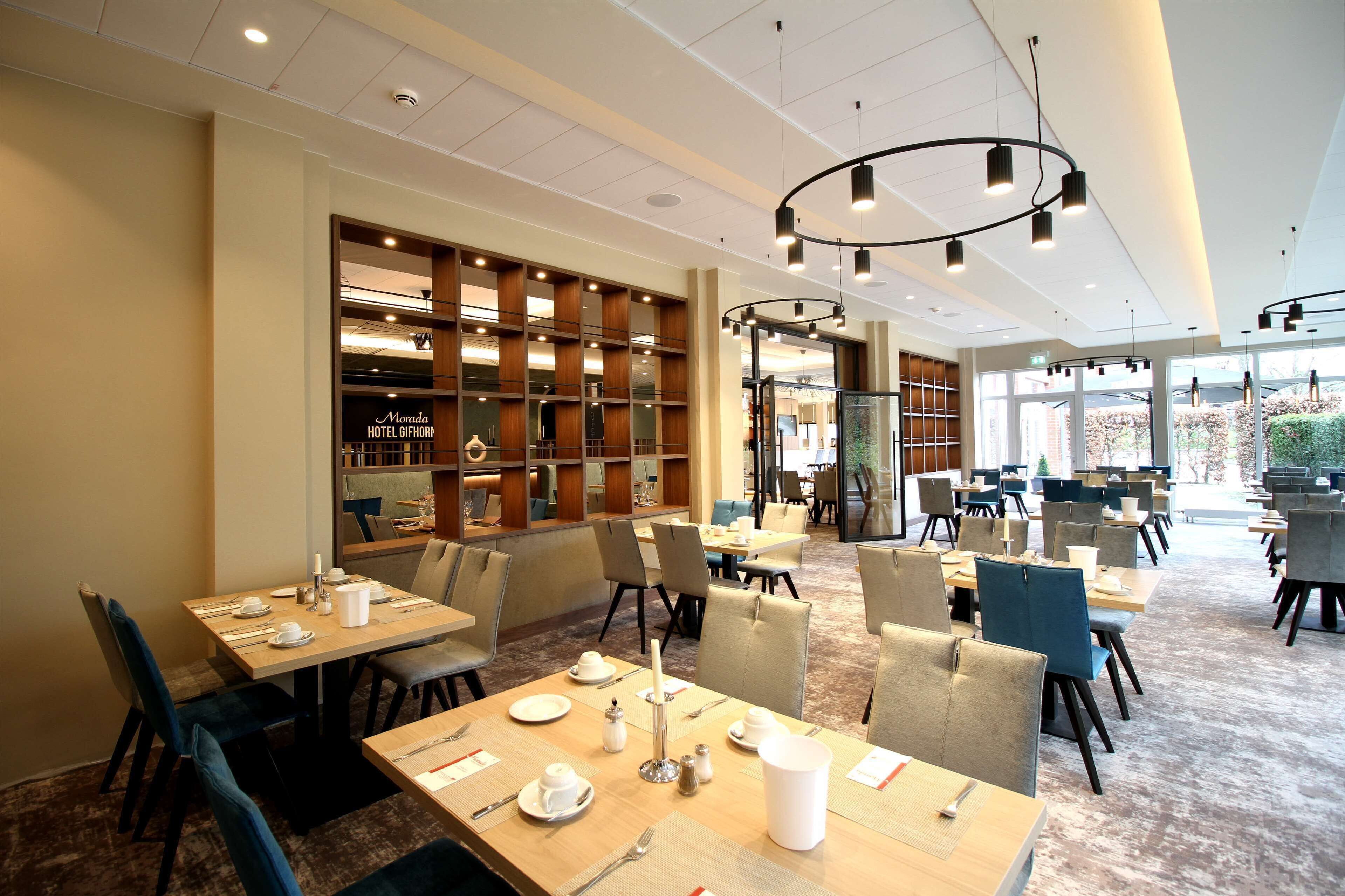Un espace de restauration d’hôtel comprenant plusieurs tables et chaises, une grande bibliothèque et un lustre moderne.