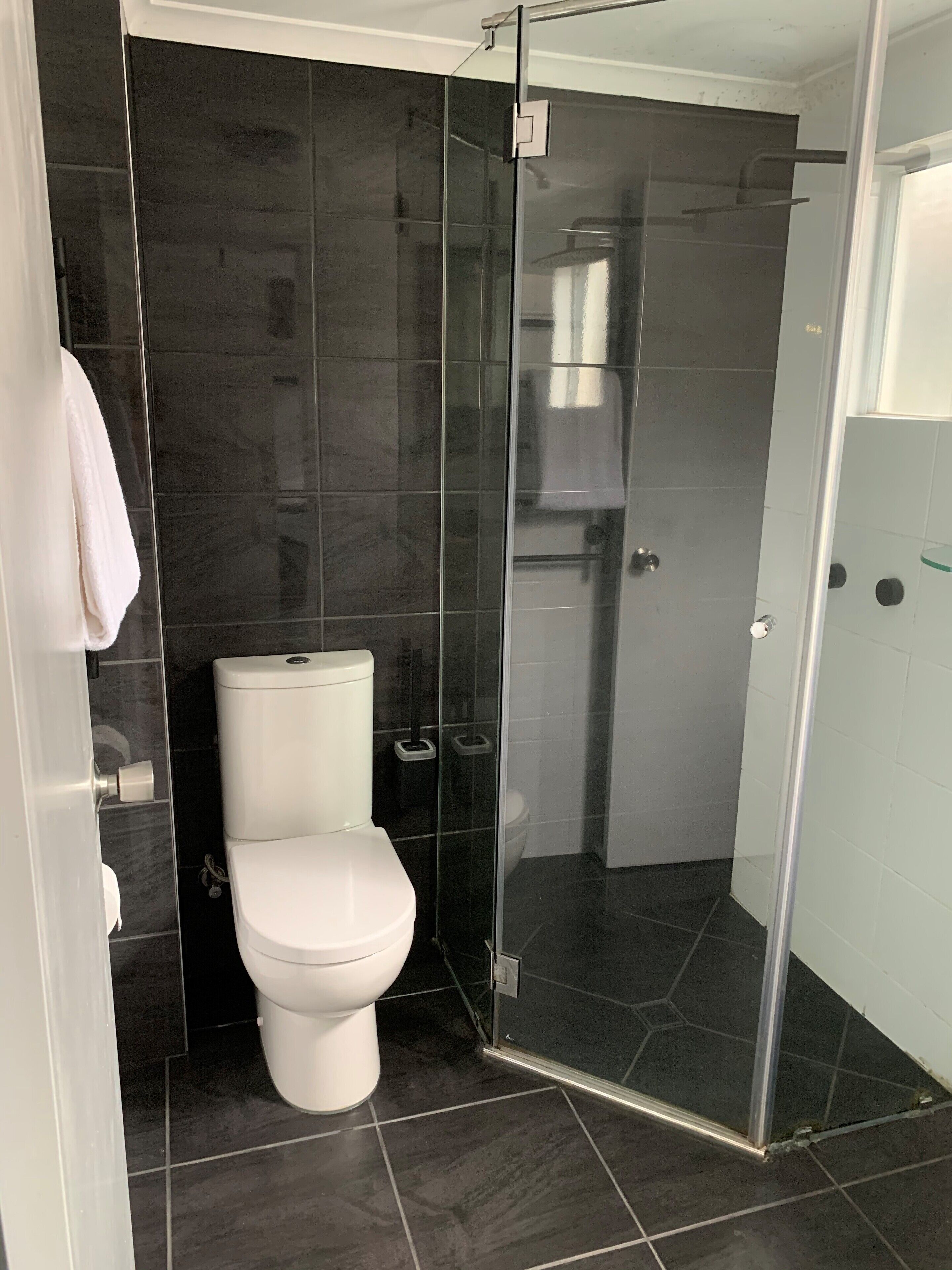 Een badkamer met een toilet, een douchecabine van glas en een handdoek aan een deurklink.