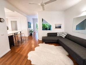 A modern living room with a grey sectional sofa, a white shag rug, a ceiling fan, and a view of greenery through a window.