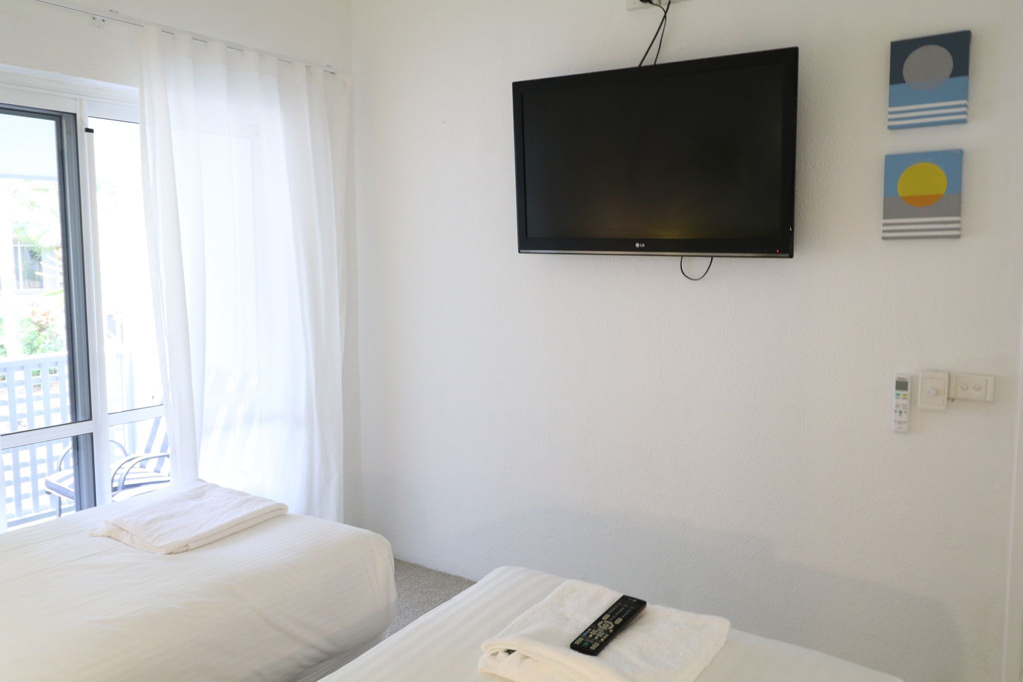 Habitación de hotel con cama, televisión montada en la pared y balcón con vistas.
