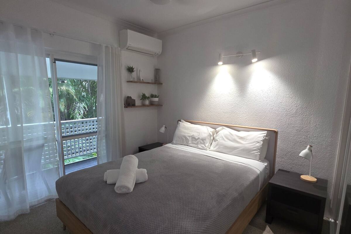 A bedroom with a bed, bedside tables, a ceiling fan, and a view of the outdoors.