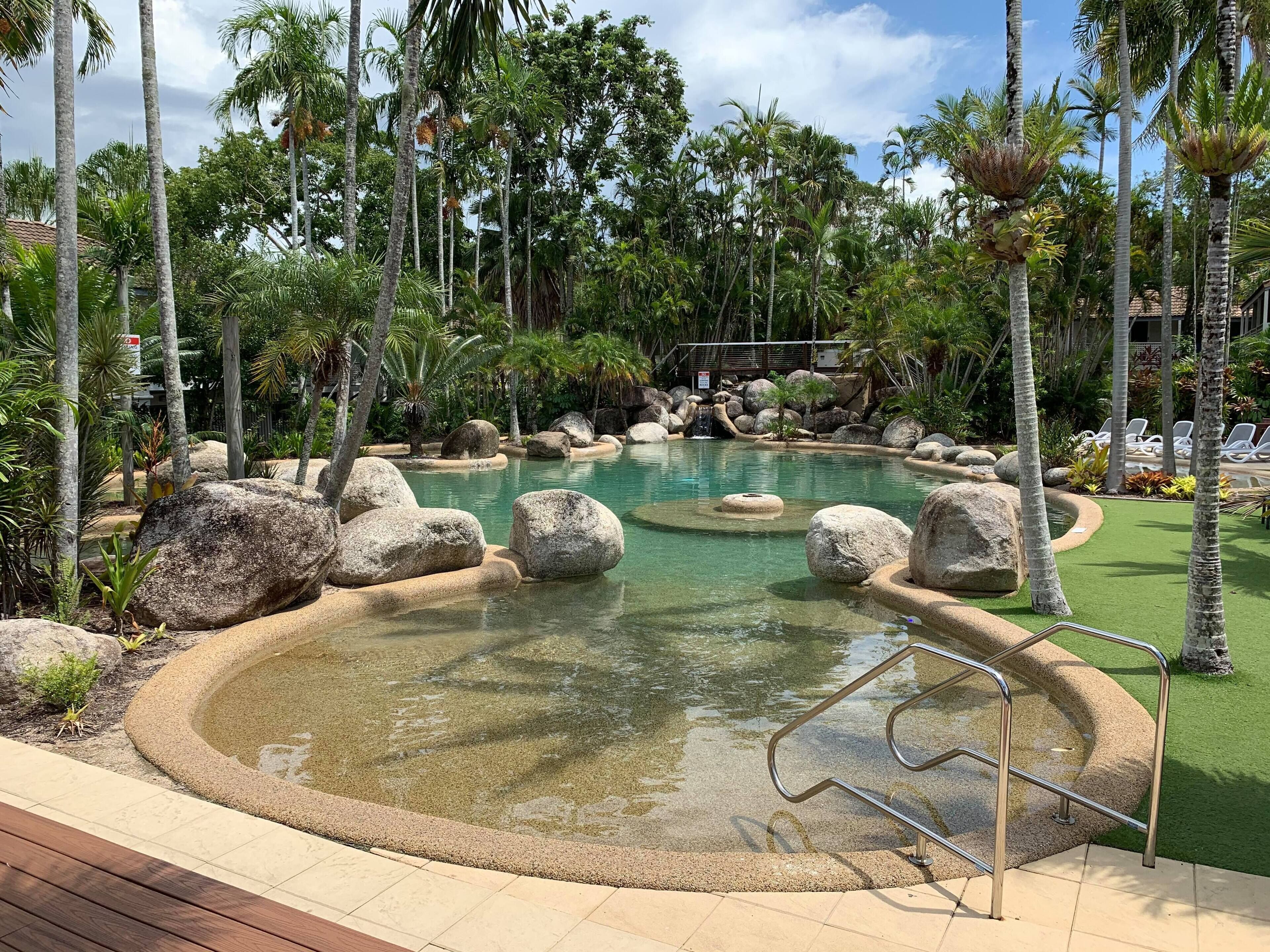 Een tropisch resort zwembad, omgeven door palmbomen en grote rotsen.