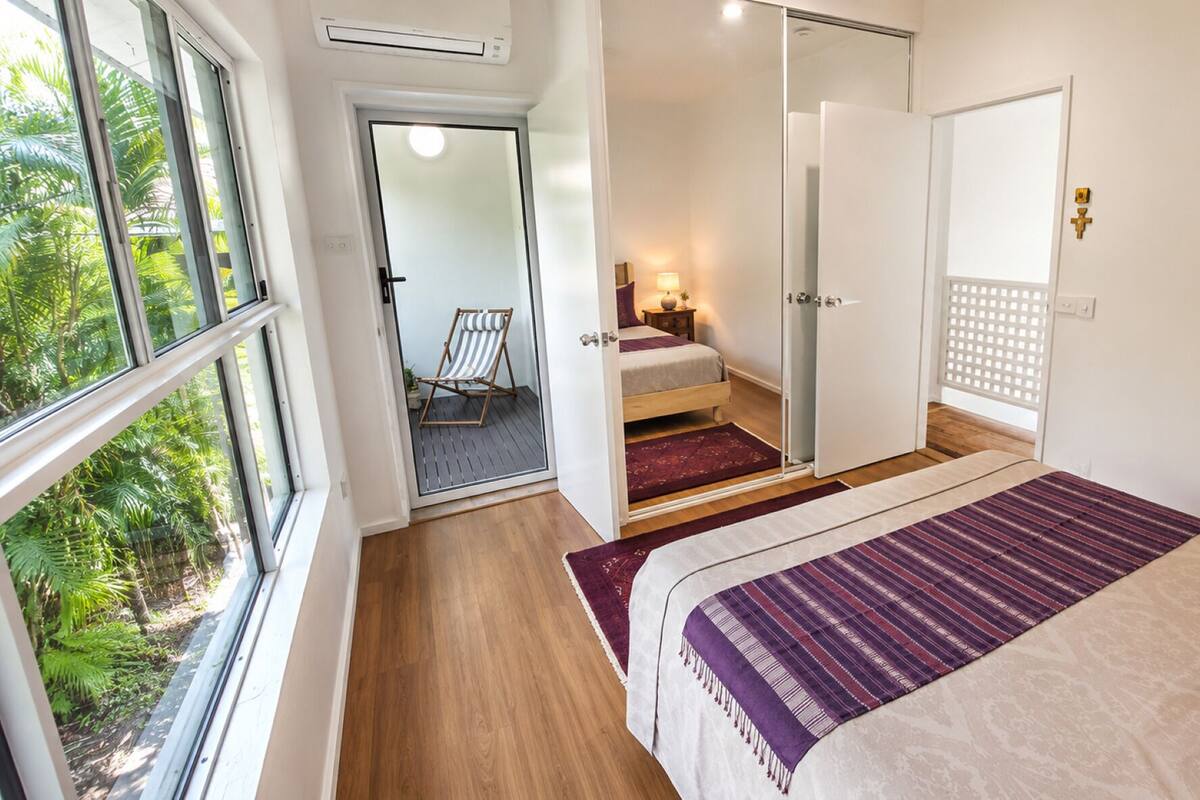 A bedroom with a bed, a window, a door, and a view of greenery outside.