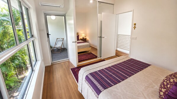 Un dormitorio con cama, ventana, puerta y vistas al exterior con vegetación.