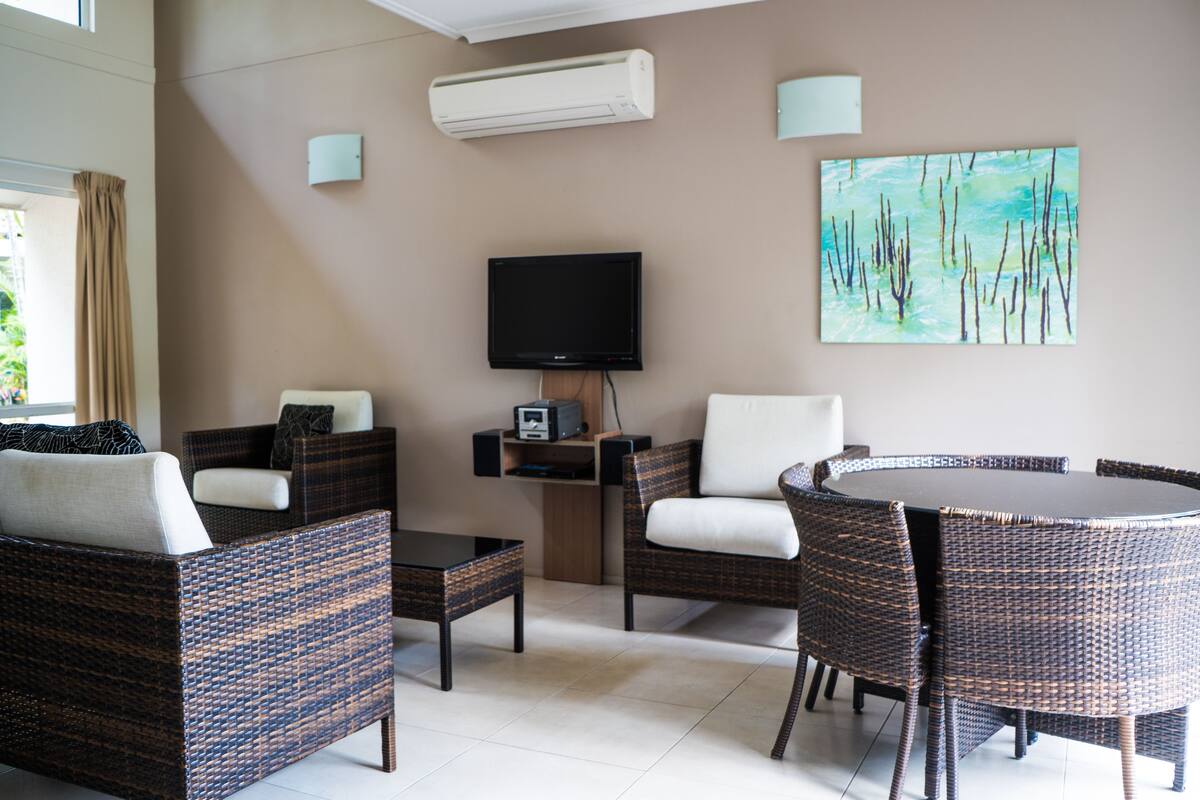 A living room with wicker furniture, a flat-screen TV, and a painting on the wall.