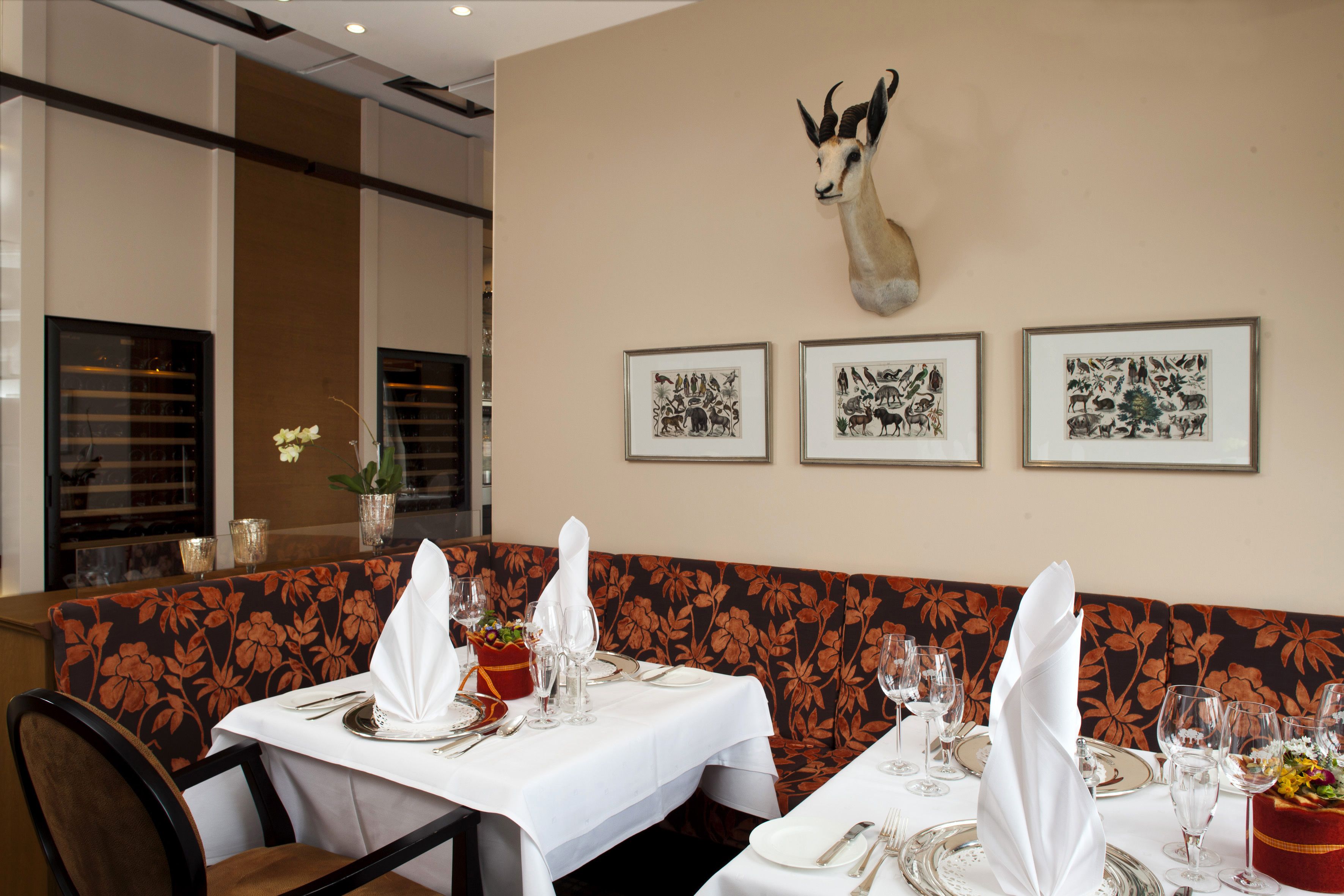 A restaurant interior with a floral-patterned booth, tables set with white tablecloths, and framed animal illustrations on the wall.