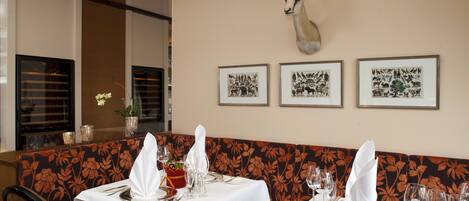 A restaurant interior with a floral-patterned booth, tables set with white tablecloths, and framed animal illustrations on the wall.