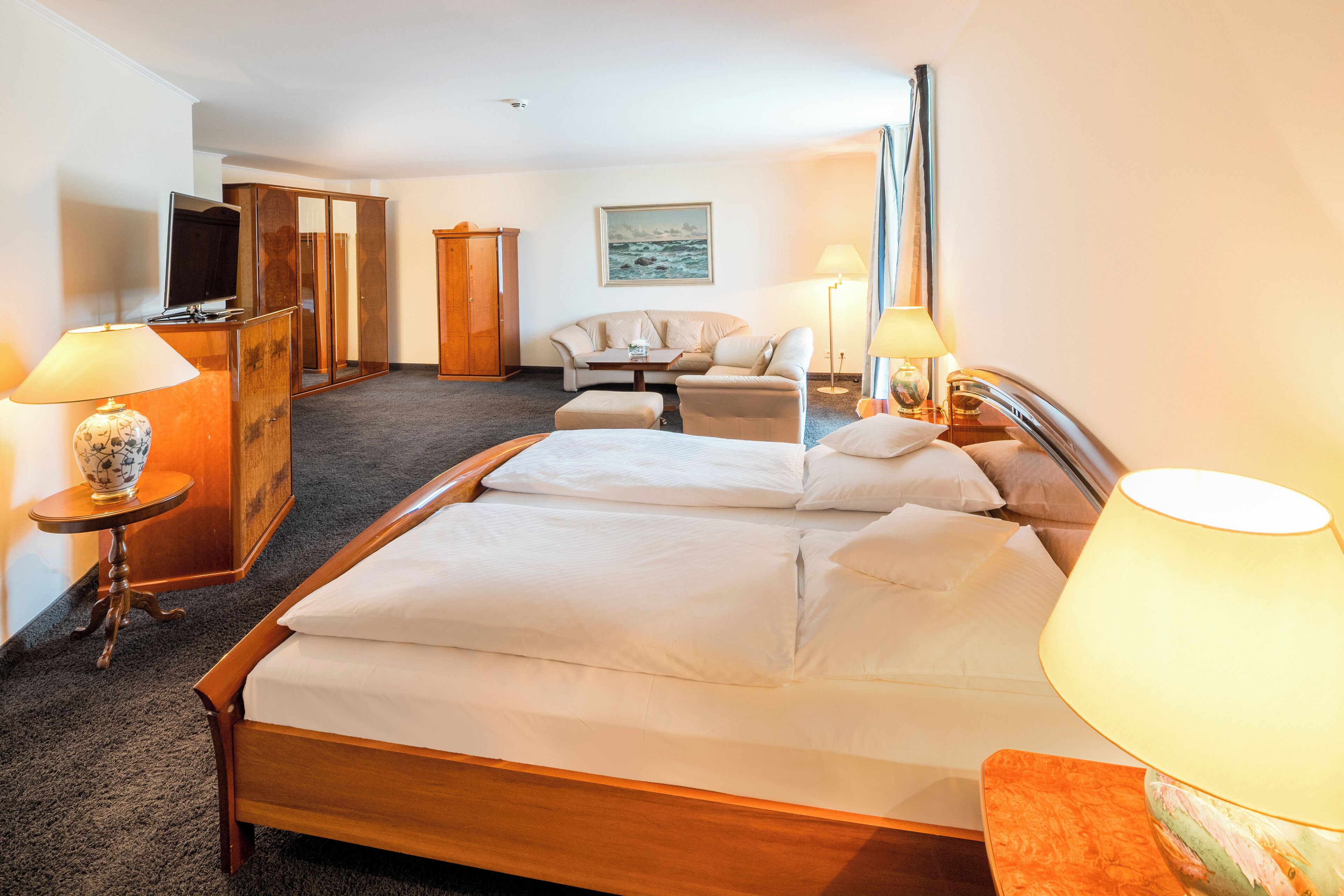 A hotel room with a large bed, a television, a desk, and a sofa.