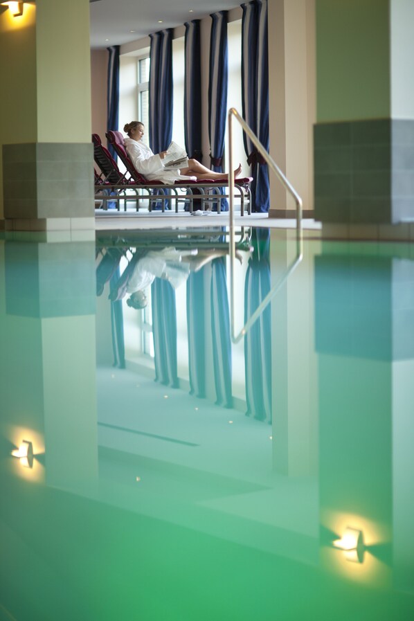 A pool area with a person reading a book, a chair, and a railing.