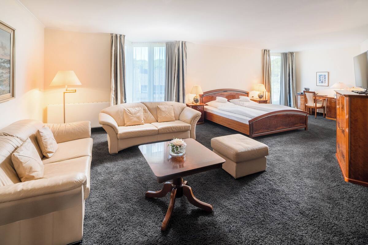 A hotel room with a bed, two sofas, a coffee table, a desk, and a TV.