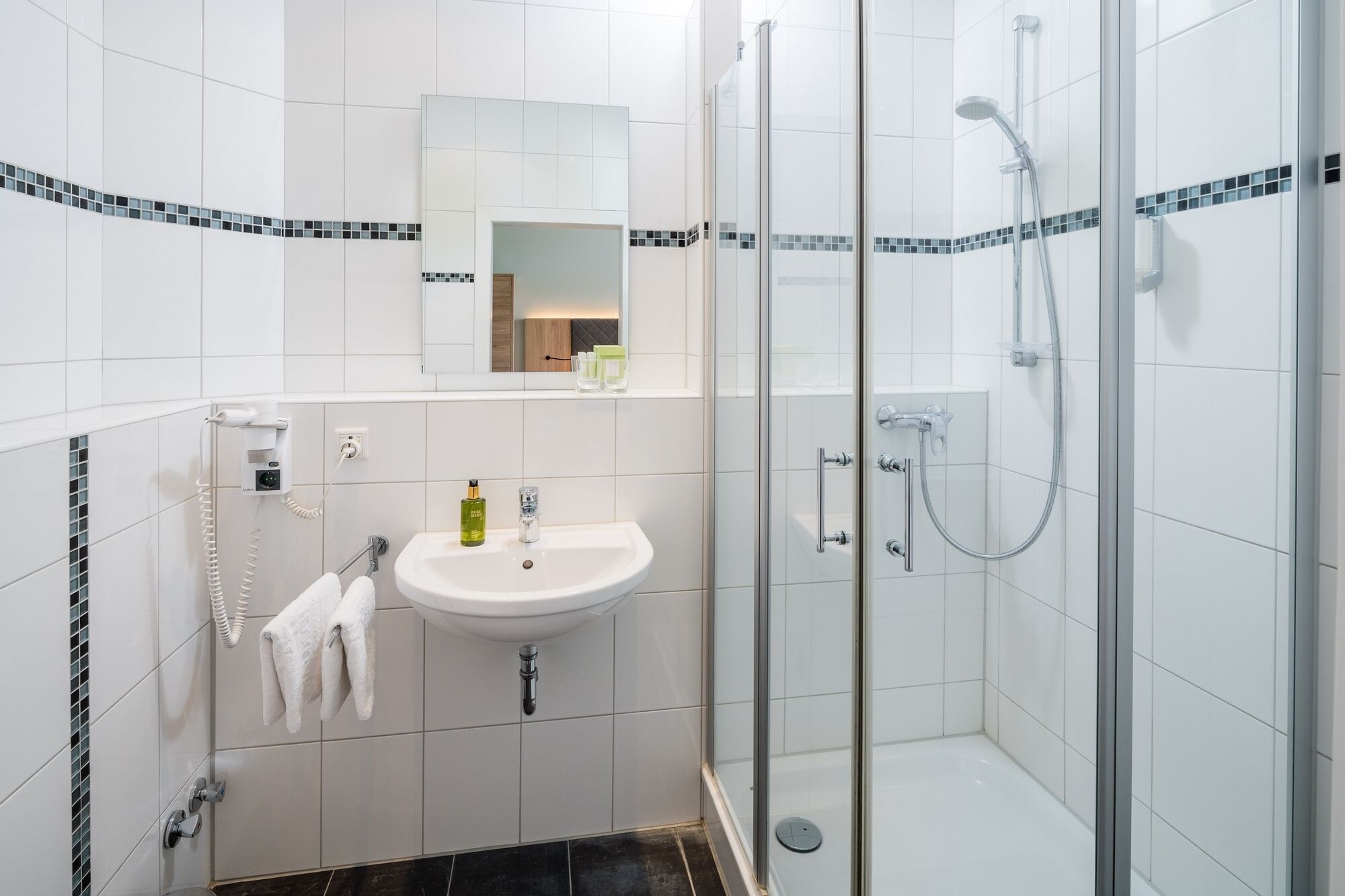 A modern bathroom with a white sink, a glass shower enclosure, and a towel hanging on a rack.