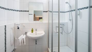 A modern bathroom with a white sink, a glass shower enclosure, and a towel hanging on a rack.