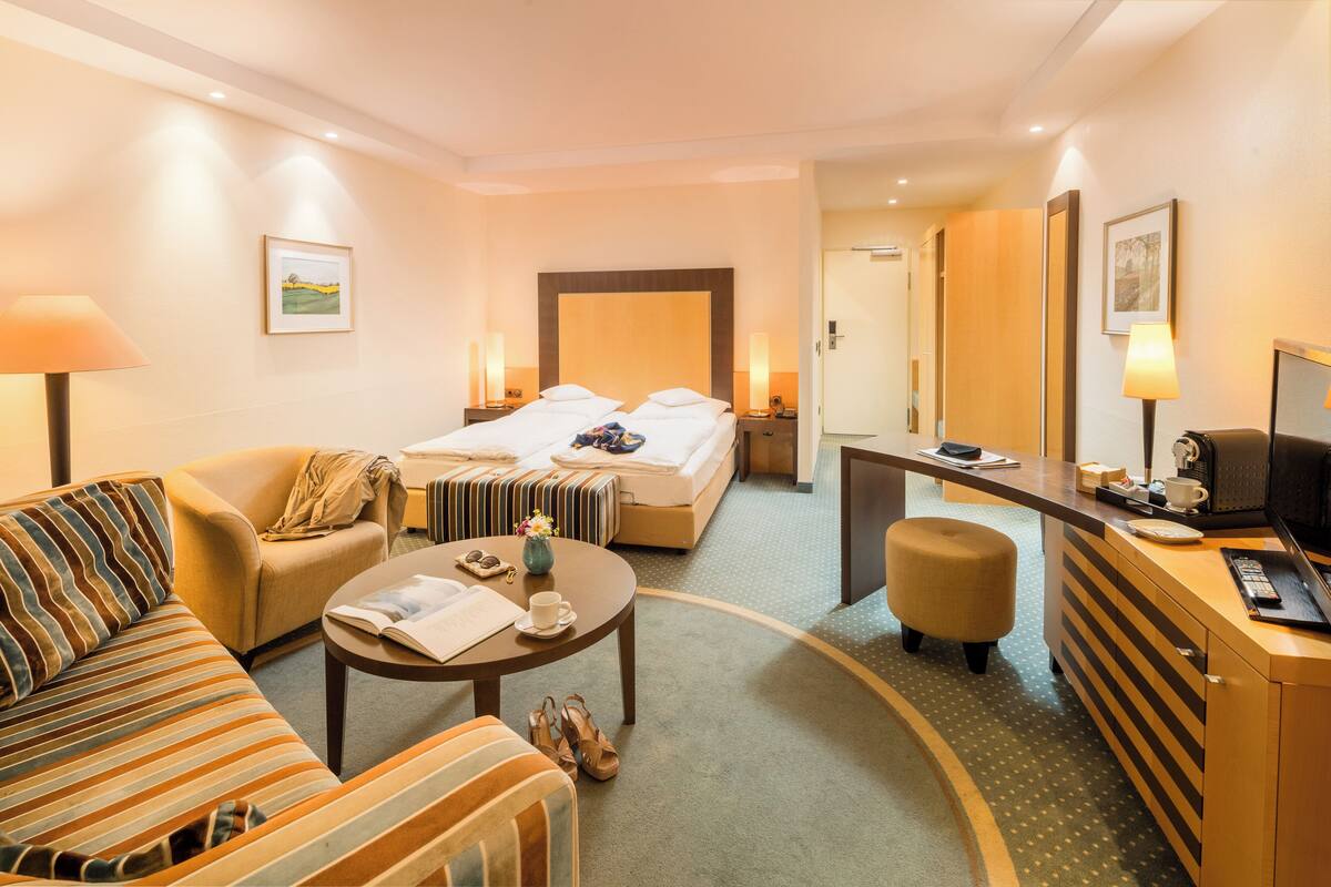 A hotel room with a bed, a sofa, a desk, a chair, a coffee table, and a TV.