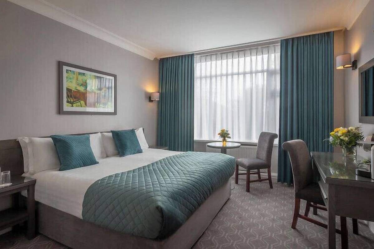Une chambre d’hôtel avec un grand lit, un bureau avec une chaise, une petite table ornée de fleurs et un tableau accroché au mur.