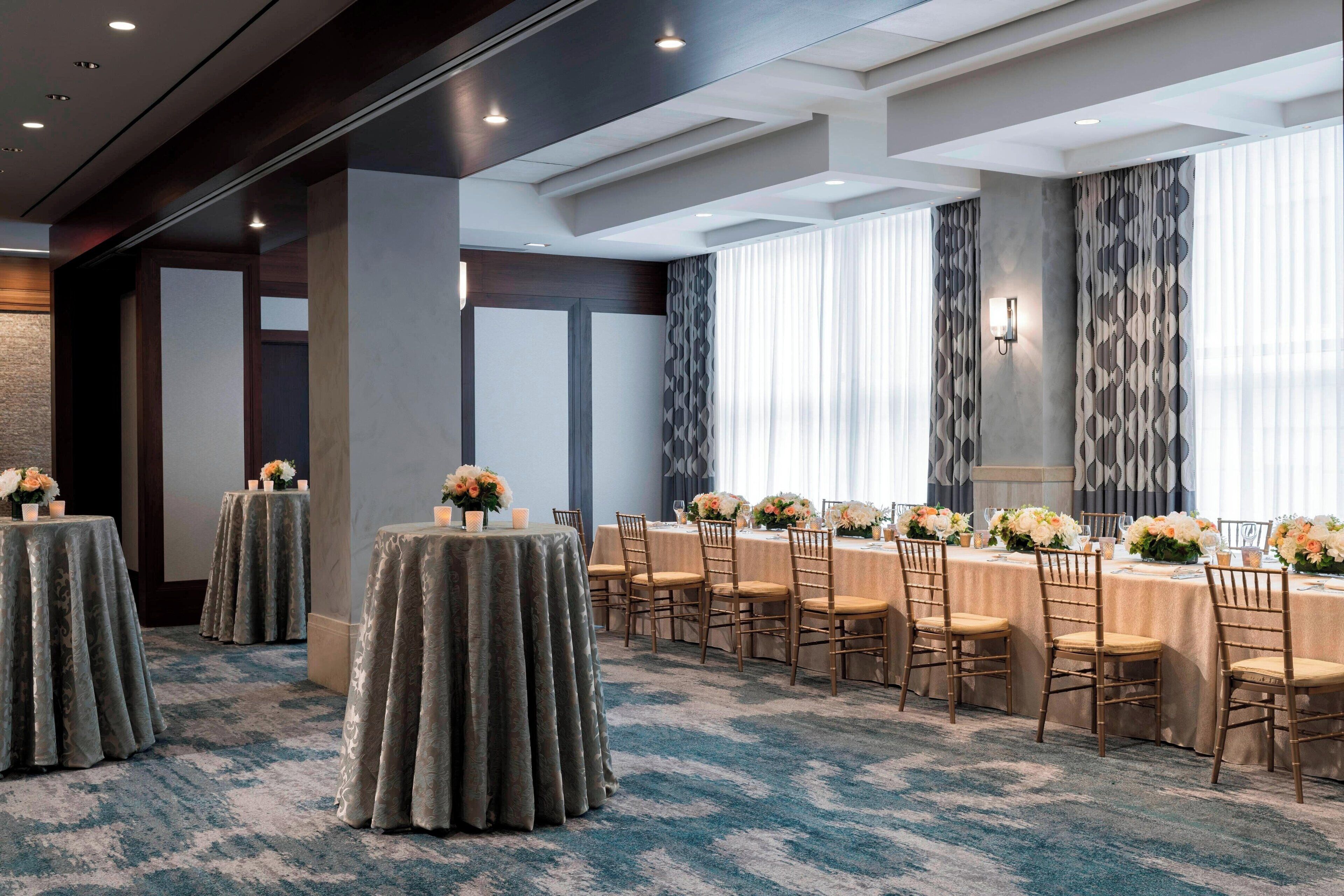 Une salle de conférence équipée de tables rondes, de chaises et agrémentée de compositions florales.