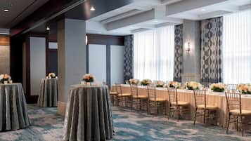 Une salle de conférence équipée de tables rondes, de chaises et agrémentée de compositions florales.