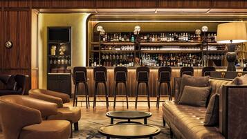 A bar area with leather chairs, a sofa, and a bar counter stocked with bottles.