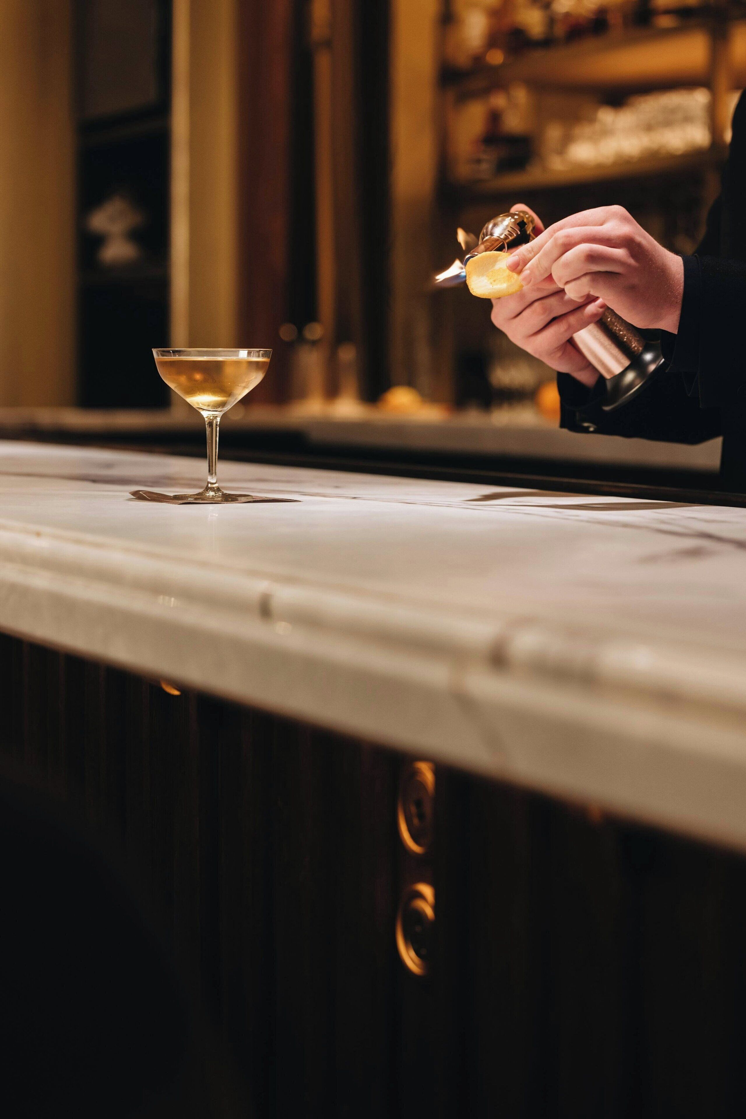 A bar setting with a martini glass and a person using a jigger.