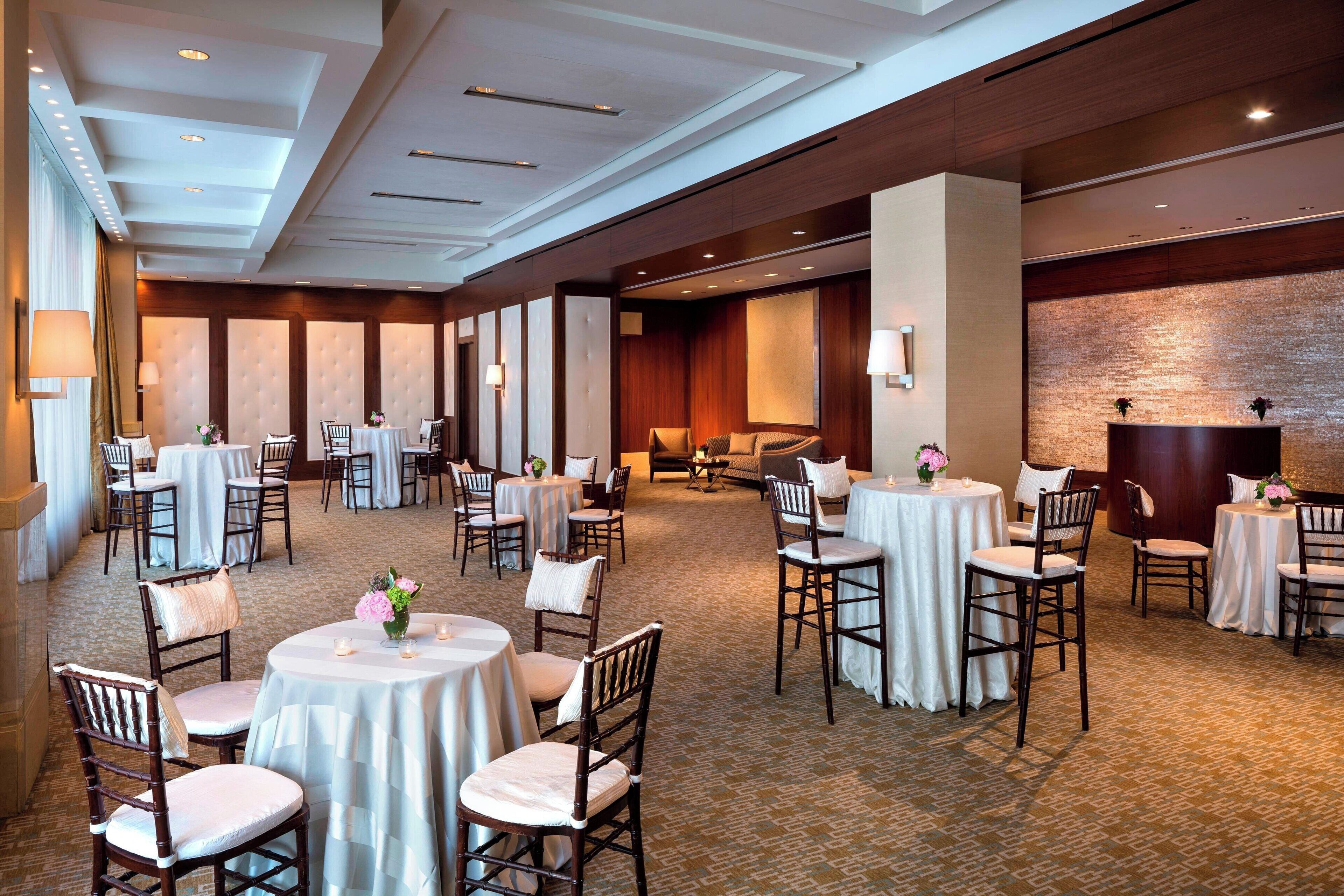 Une salle à manger d’hôtel avec des tables et des chaises rondes, une moquette à motifs et un mur en briques.