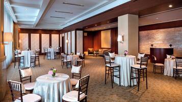 Une salle à manger d’hôtel avec des tables et des chaises rondes, une moquette à motifs et un mur en briques.