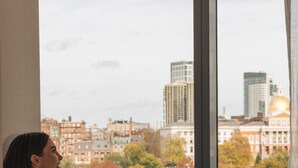 A person sitting by a window with a cityscape view, a breakfast tray, and a cup.