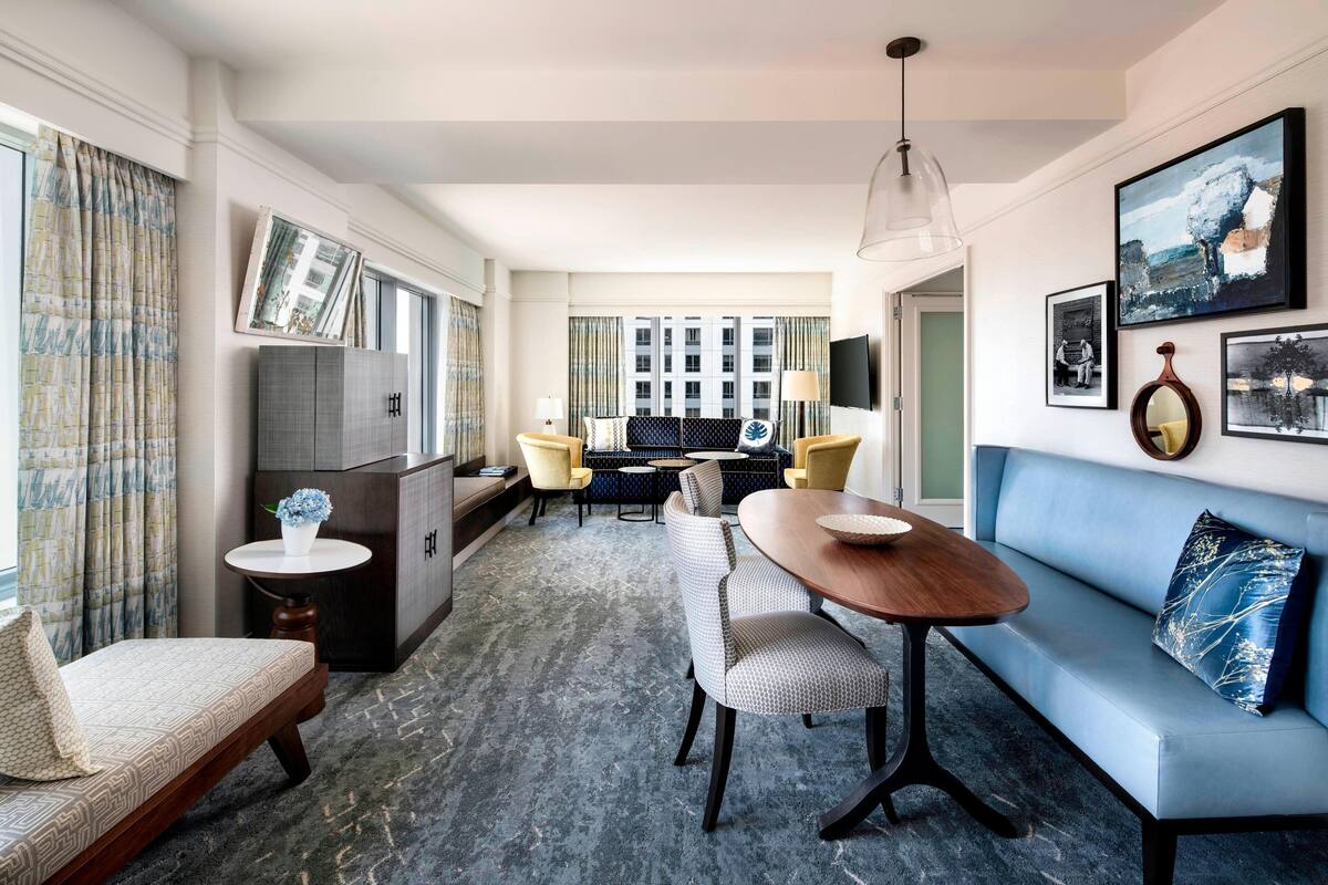 Une chambre d’hôtel moderne équipée d’un canapé, d’une table à manger, de chaises, d’une petite table d’appoint et d’un téléviseur.