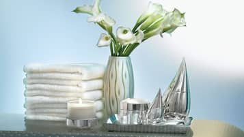 A stack of white towels, a vase with white flowers, and a silver decorative item on a reflective surface.