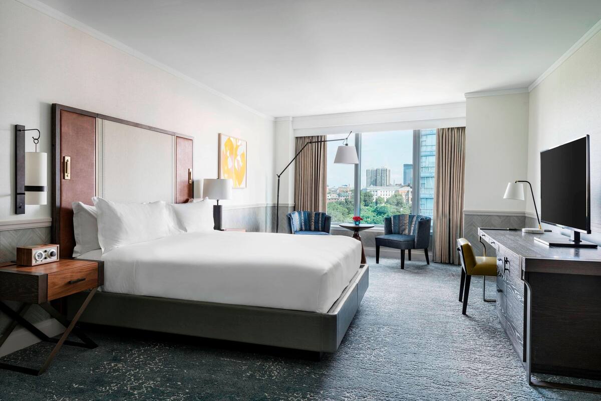 Une chambre d’hôtel avec un grand lit, un bureau, une chaise, une télévision et une vue sur la ville.