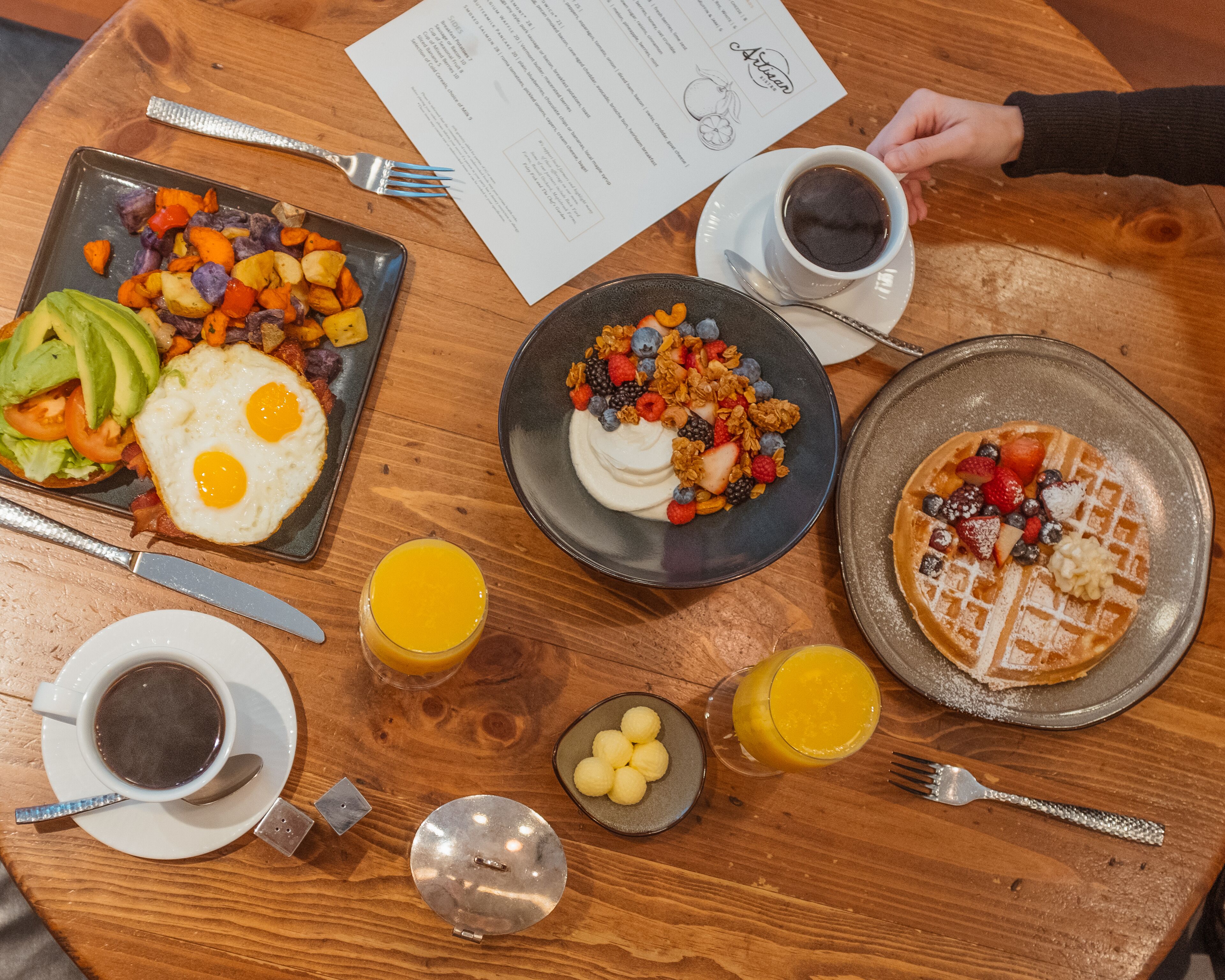 Una mesa de desayuno con diversos platos, como huevos, gofres y fruta.