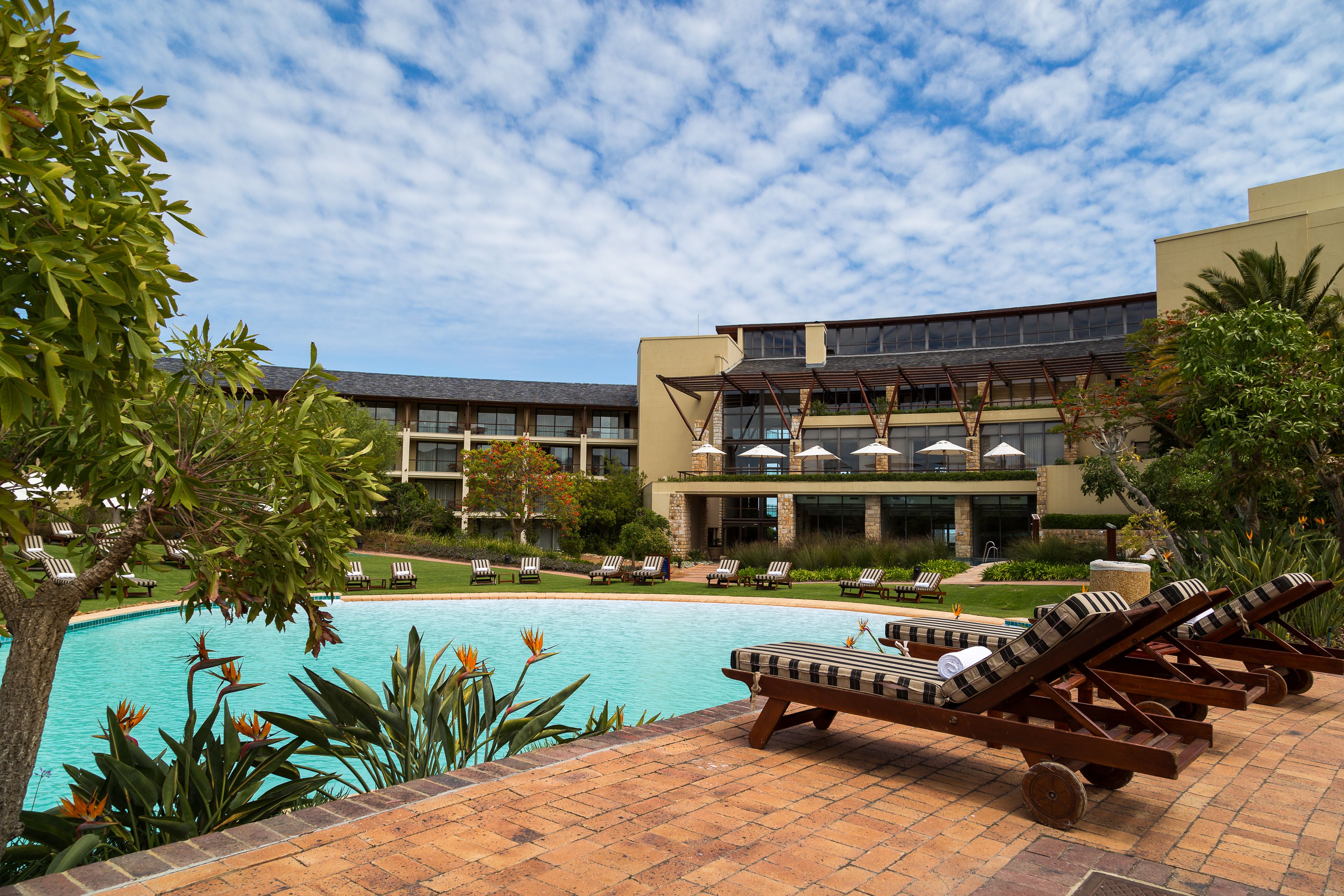 A pool area with lounge chairs, a building with multiple floors, and a clear sky.