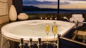 A modern bathroom with a large bathtub, two glasses of champagne, and a view of the ocean at sunset. - Arabella Hotel Golf & Spa (Kleinmond)