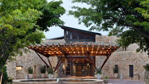 A modern building with a stone facade, a covered entrance with lights, and a circular water feature. - Arabella Hotel Golf & Spa (Kleinmond)