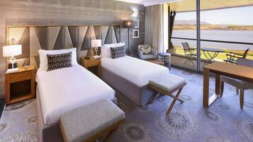 A hotel room with two beds, a dining table, and a view of a body of water.