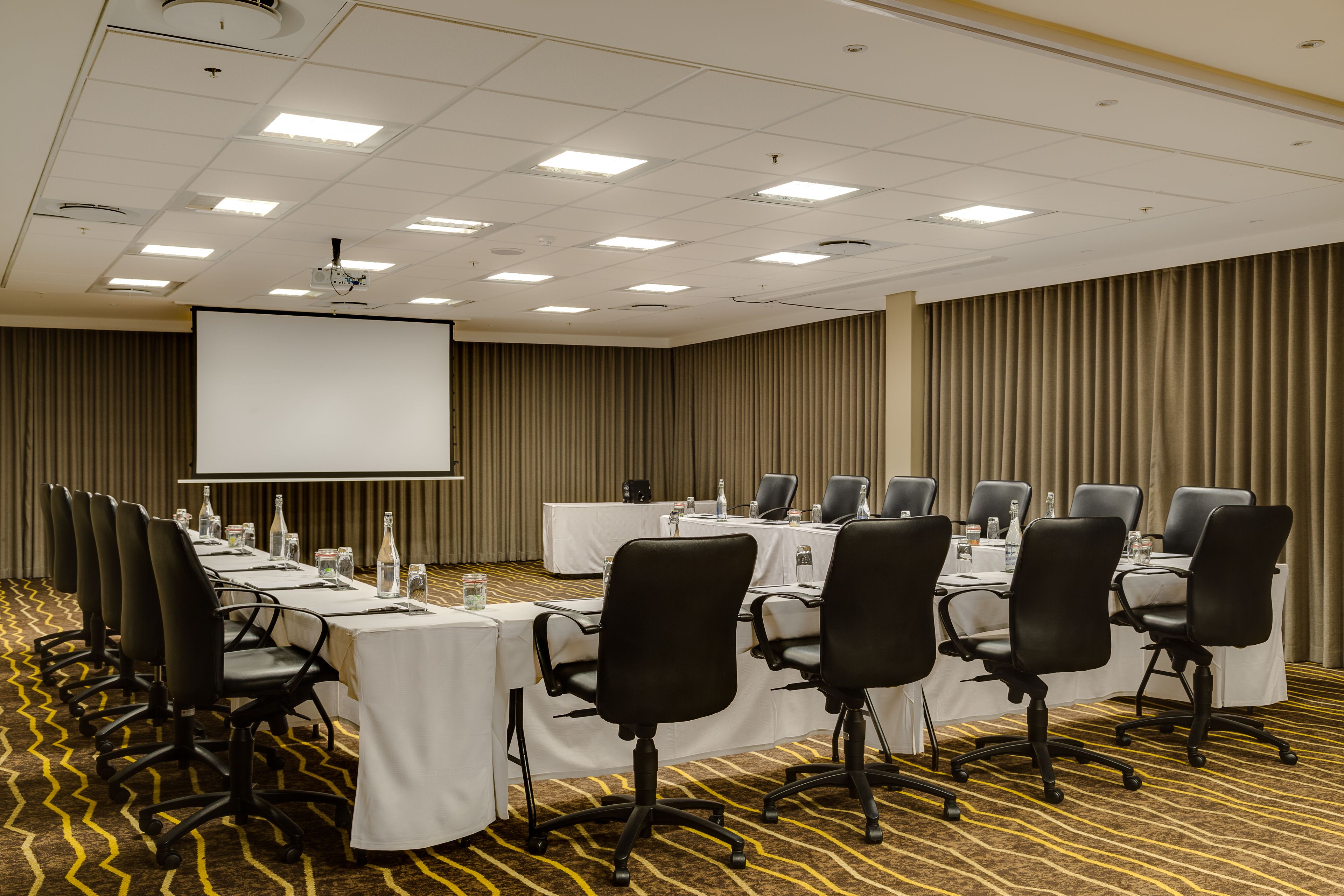 Une salle de conférence équipée d’une longue table, de chaises, d’un écran de projection et d’un tableau blanc.