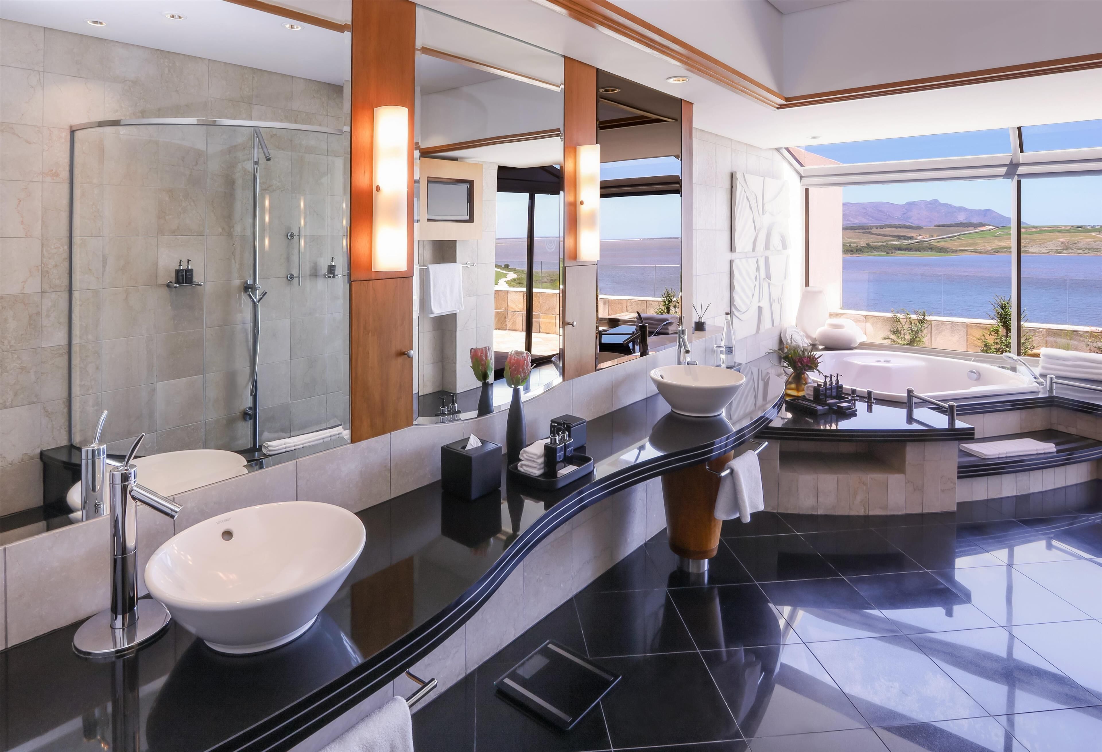 A modern bathroom with a large mirror, two sinks, a shower, and a bathtub.