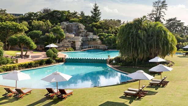 A swimming pool with a waterfall feature, surrounded by lounge chairs and umbrellas. - Arabella Hotel Golf & Spa (Kleinmond)