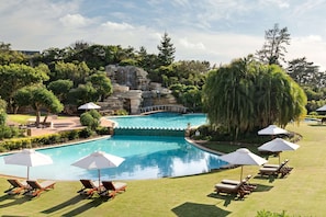 Una piscina con una cascada, rodeada de sillones y sombrillas.