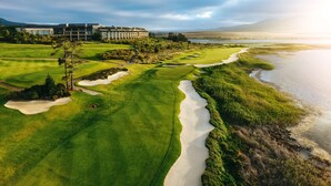 A golf course with bunkers and a water hazard, a building in the background, and a clear sky. - Arabella Hotel Golf & Spa (Kleinmond)