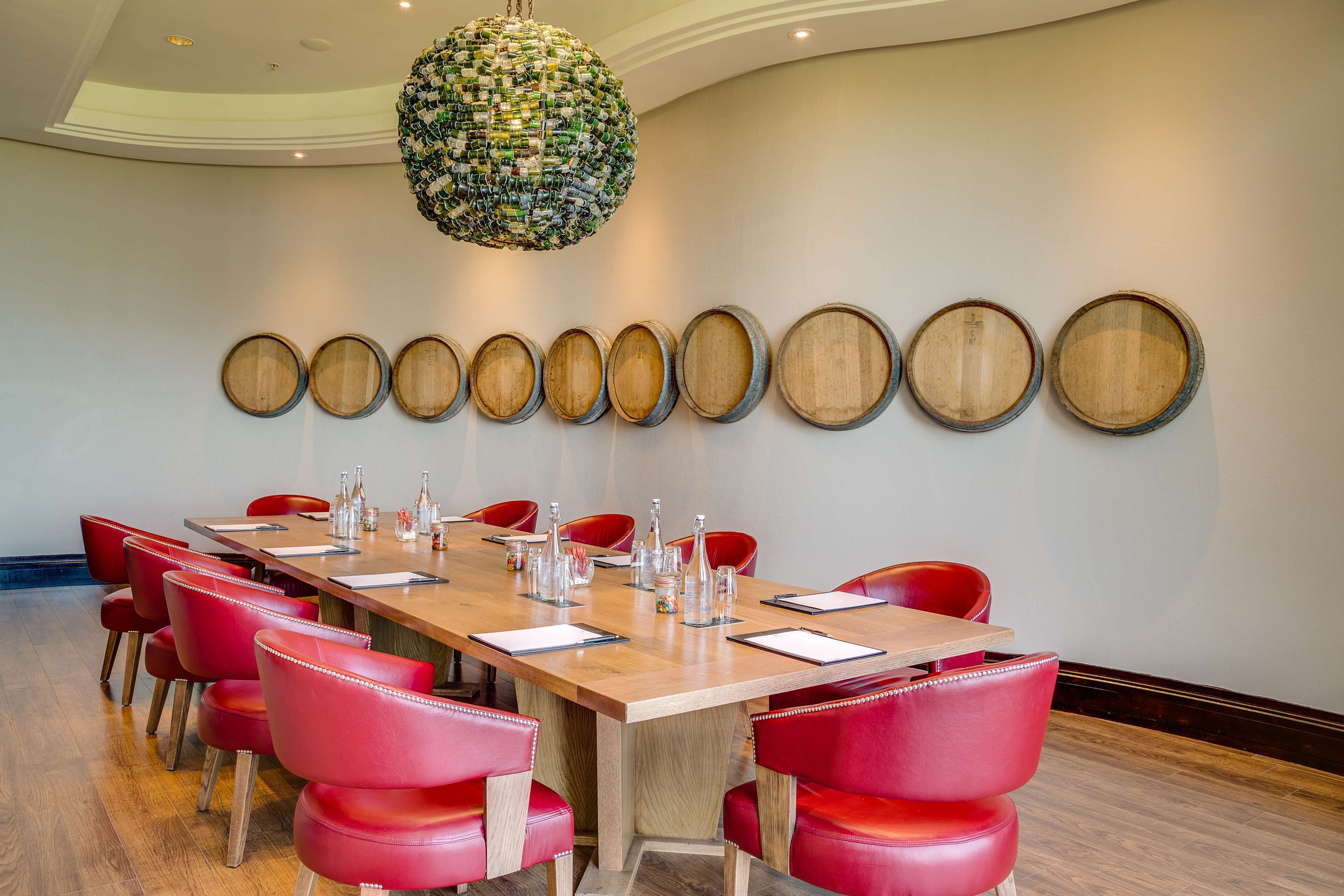 A conference room with a long wooden table, red chairs, and a decorative wall with wooden panels.
